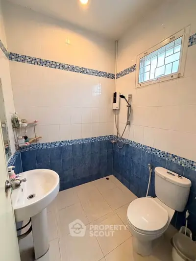 Modern bathroom with blue and white tiles, featuring a shower, sink, and toilet.