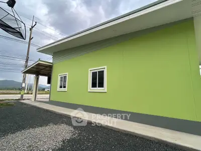 Modern green exterior of a single-story building with mountain views, showcasing sleek design and ample natural light.