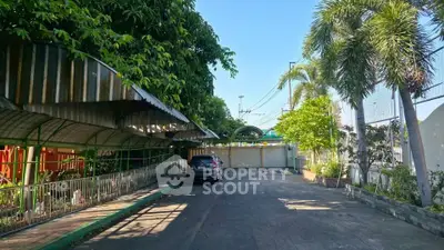 Spacious driveway with lush greenery and secure gated entrance in a tropical setting.