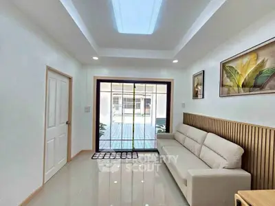 Bright living room with modern sofa and large window overlooking patio, featuring elegant wall art and sleek flooring.
