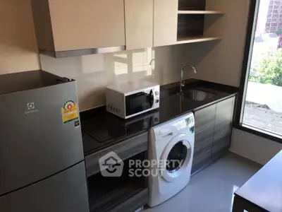 Modern kitchen with sleek appliances including fridge, microwave, and washing machine, featuring ample storage.