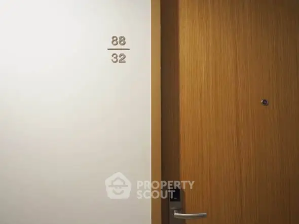 Modern apartment entrance with sleek wooden door and room number 88/32 displayed on the wall.