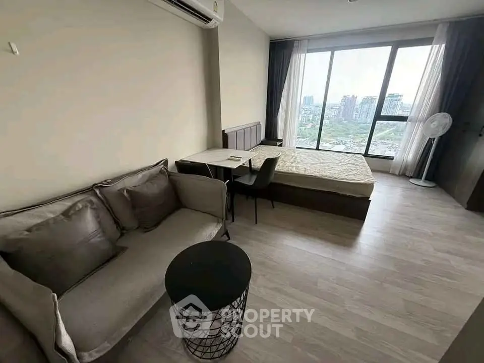 Modern studio apartment with large window and city view, featuring cozy sofa and bed.