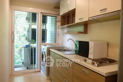 Modern kitchen with washing machine and microwave, featuring sleek cabinetry and natural light.