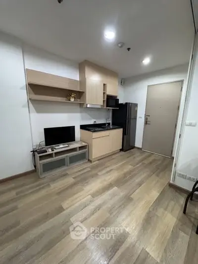 Modern apartment interior with sleek kitchen and cozy living area, featuring wooden flooring and stylish cabinetry.