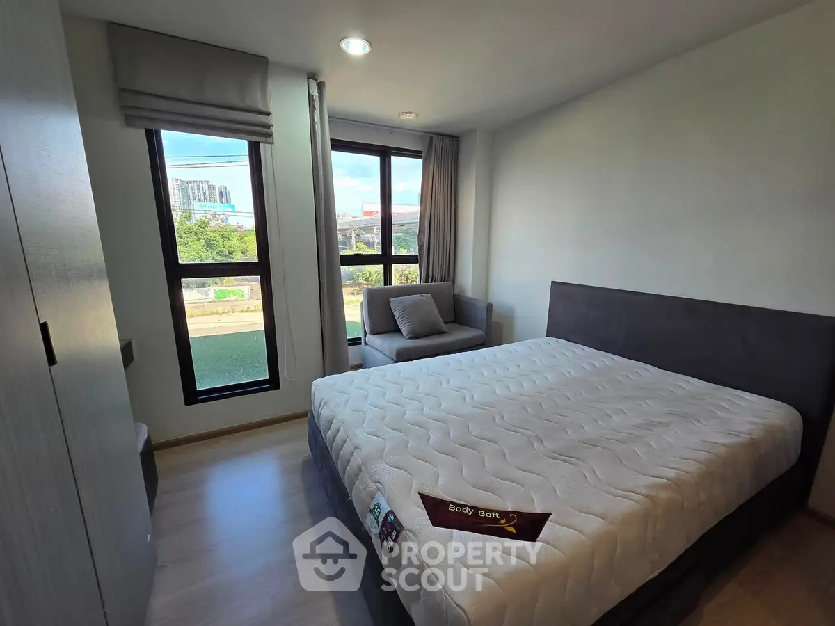 Modern bedroom with large windows and cozy seating area, offering a bright and inviting atmosphere.