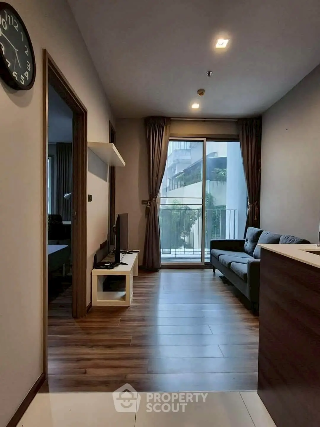 Modern living room with balcony view, sleek wooden flooring, and cozy seating area.