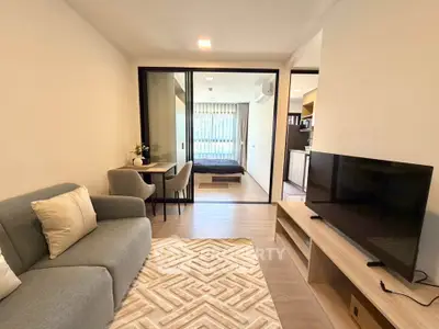 Modern open-plan living room with cozy sofa, TV, and dining area leading to a stylish bedroom.