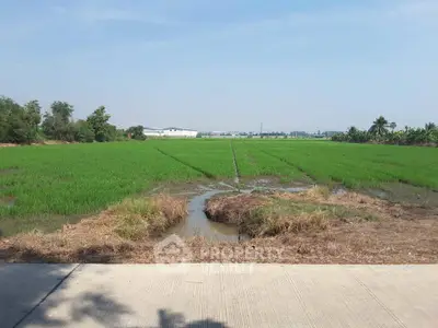 Expansive agricultural land with lush green fields and distant industrial buildings, ideal for development.