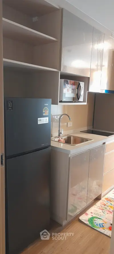 Modern kitchen with sleek cabinetry and stainless steel appliances, featuring a compact fridge and microwave.