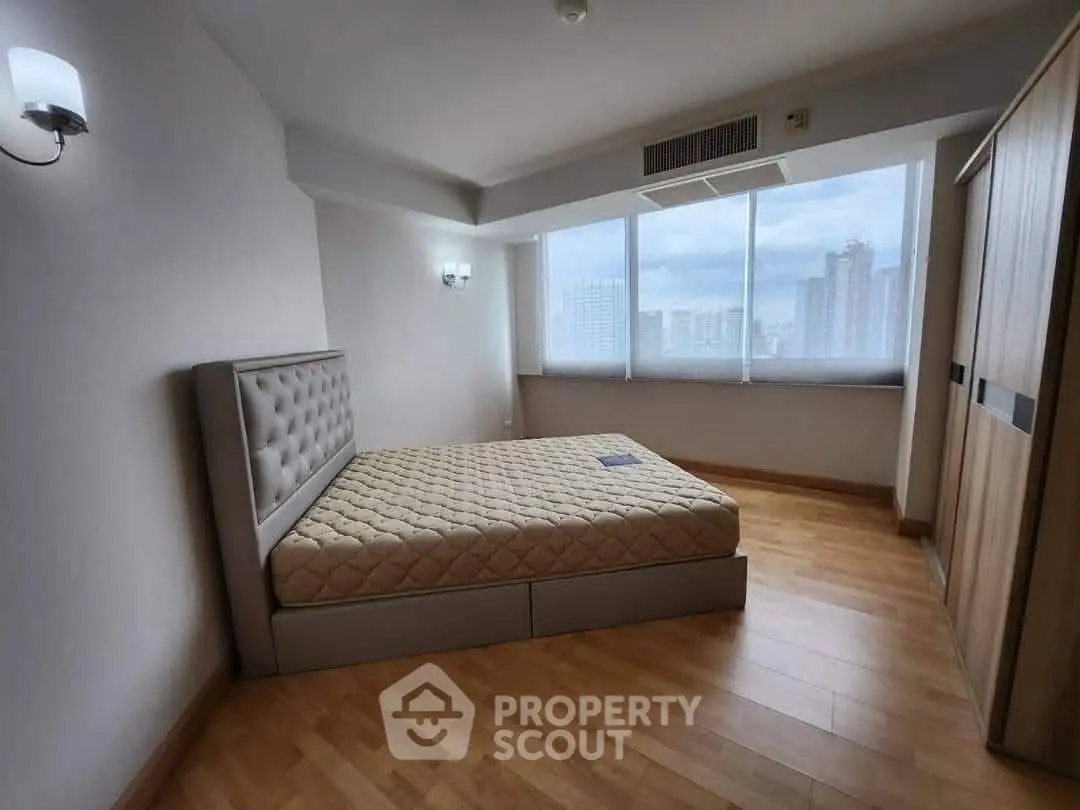 Spacious bedroom with large windows and city view in modern apartment.