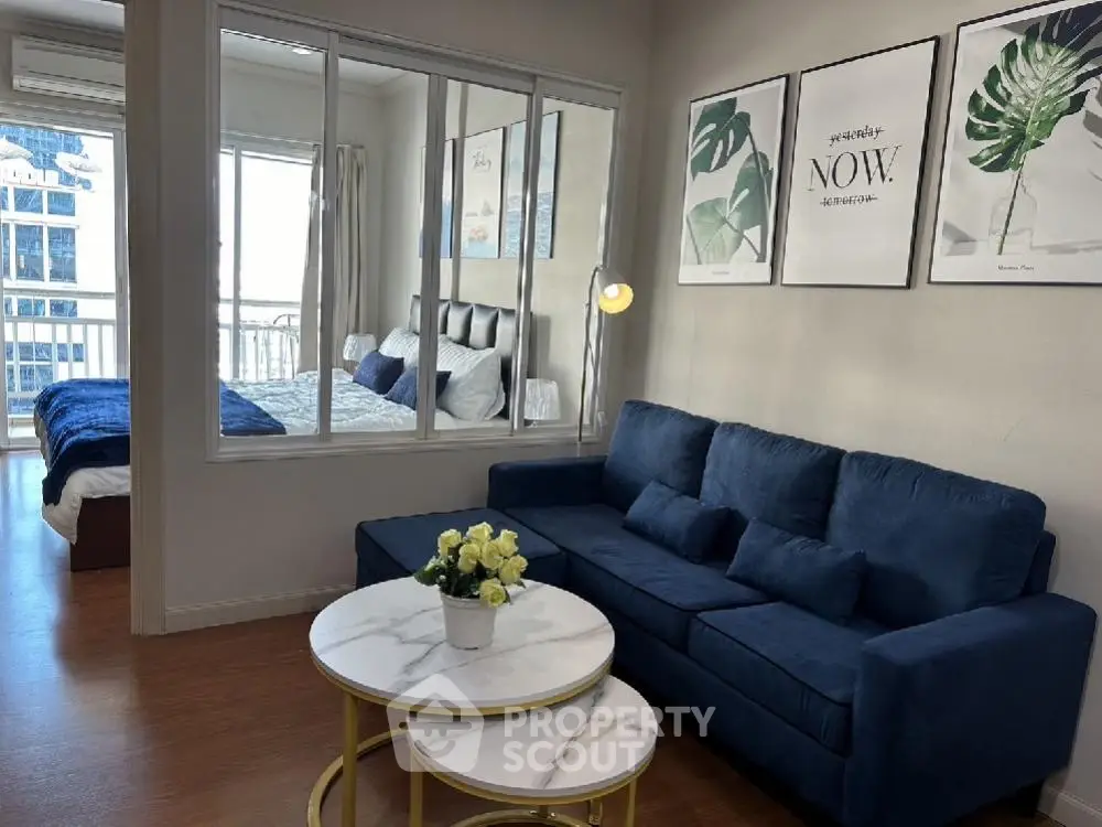 Modern living room with blue sofa and stylish decor, adjacent to a cozy bedroom with natural light.