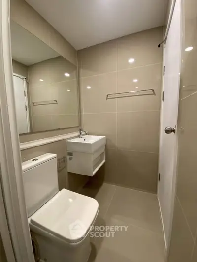 Modern bathroom with sleek fixtures and neutral tiles, featuring a wall-mounted sink and toilet.