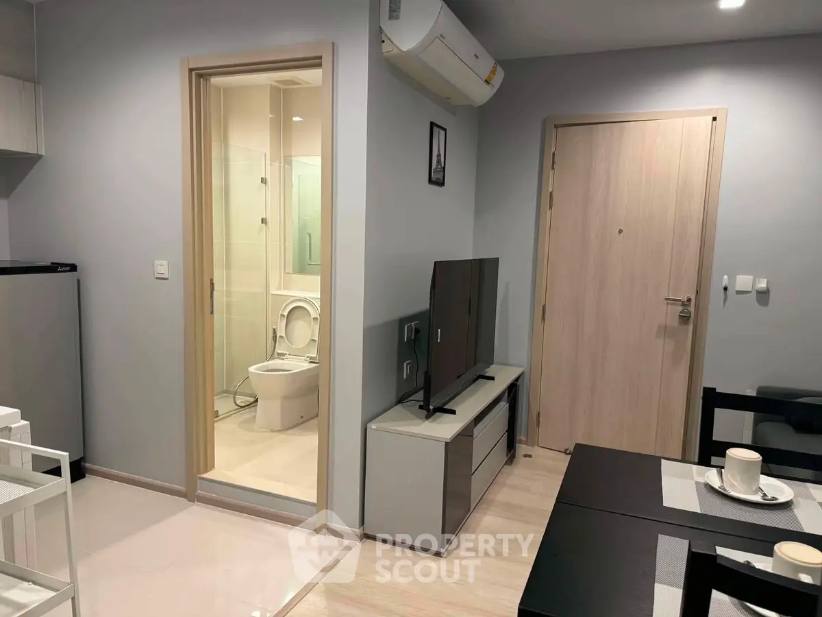 Modern apartment interior with open living area and visible bathroom, featuring sleek furniture and neutral tones.