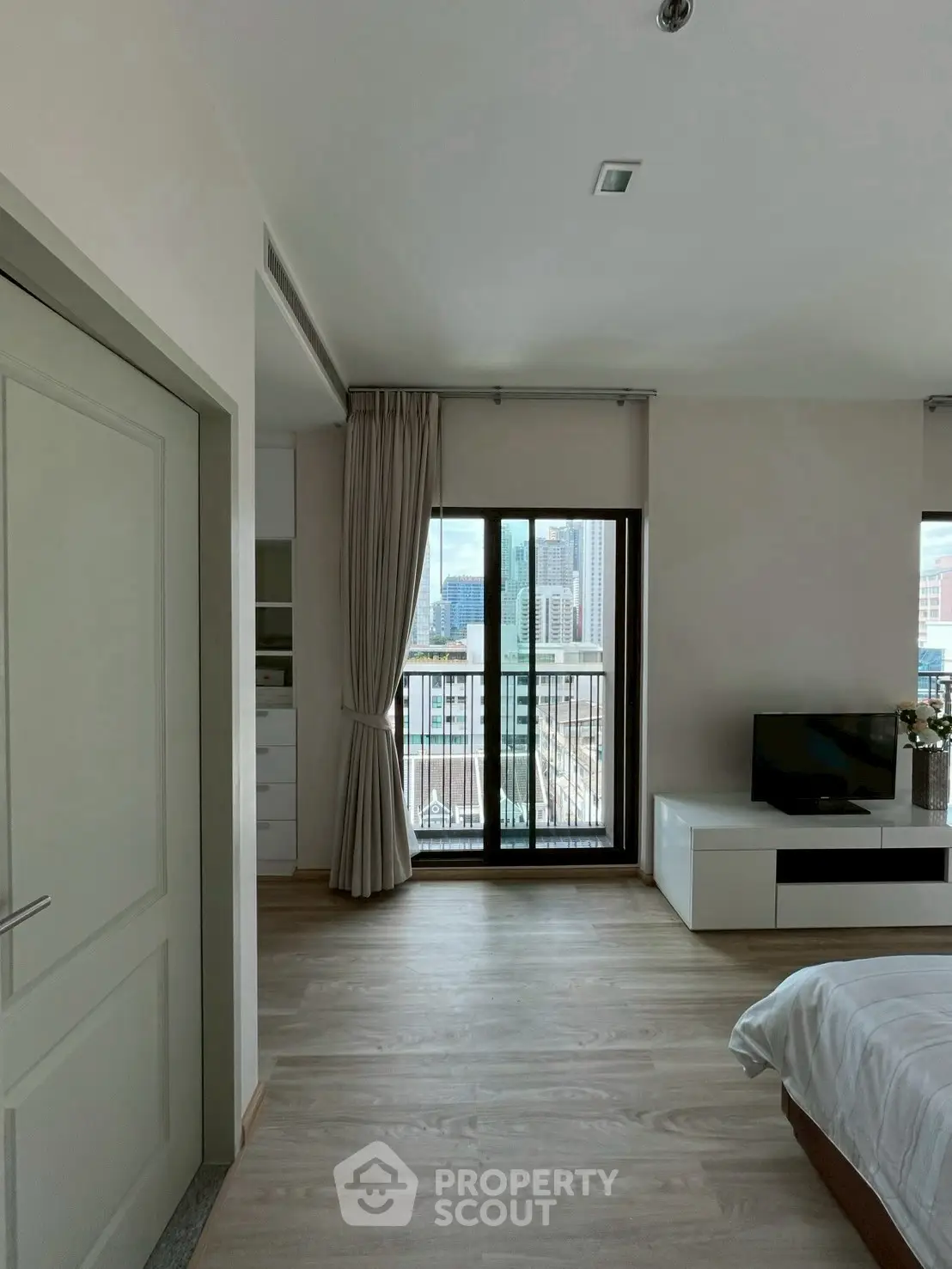 Modern bedroom with city view and balcony access, featuring sleek furnishings and natural light.