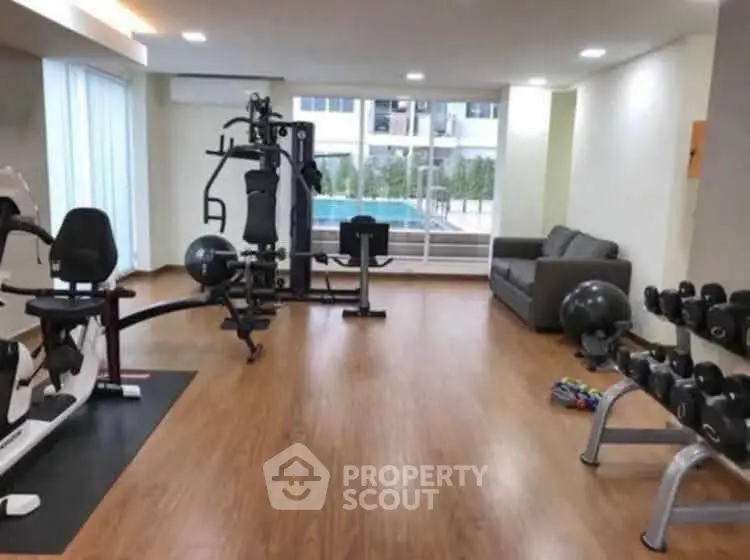 Modern gym with exercise equipment and pool view in luxury apartment complex.