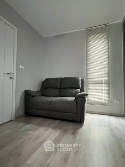 Cozy living room with modern gray sofa and natural light from window blinds.