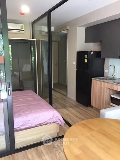 Modern studio apartment with glass partitions and compact kitchen in urban setting.