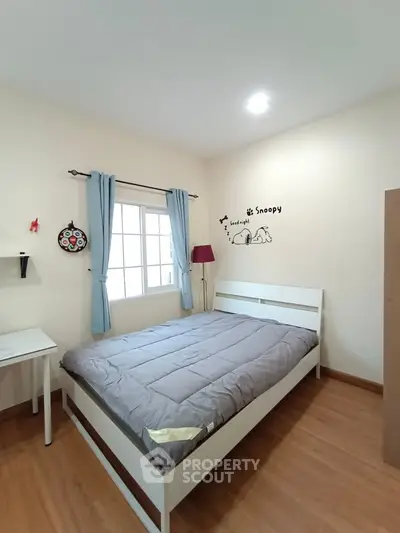 Cozy bedroom with wooden flooring and natural light, featuring a comfortable bed and stylish decor.