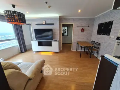 Spacious living room with modern decor and wooden flooring, featuring a large TV and comfortable seating.
