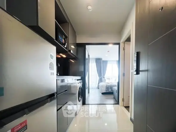 Modern apartment kitchen with sleek appliances and view into a bright bedroom.