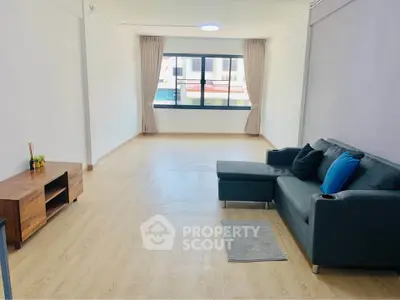 Spacious living room with modern sofa and wooden flooring, featuring large window for natural light.