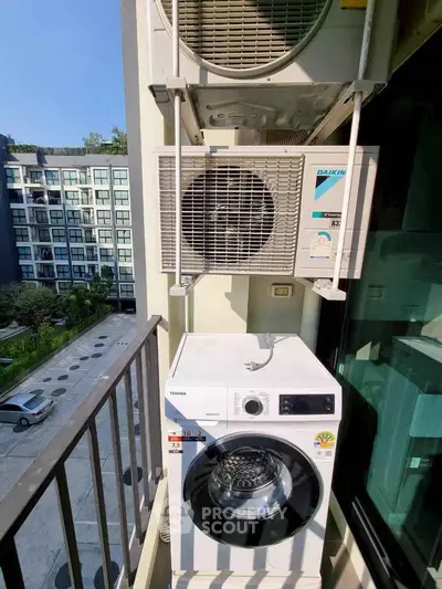 Modern apartment balcony with washing machine and air conditioning units, overlooking a residential complex.