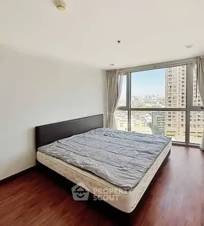 Spacious bedroom with large window offering stunning city views in modern apartment.
