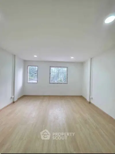 Spacious empty room with wooden flooring and large windows offering natural light.