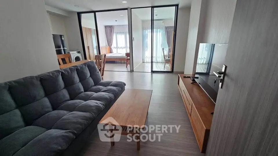 Modern living room with sleek furniture and open layout leading to a bright bedroom.