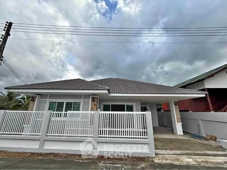 Charming single-story house with modern design and fenced yard under a cloudy sky.
