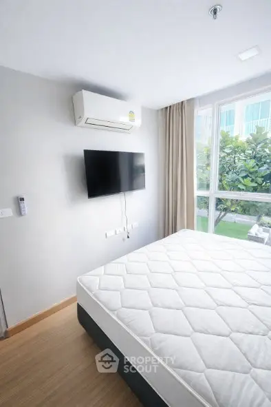 Bright bedroom with large window, air conditioning, and wall-mounted TV, perfect for modern living.
