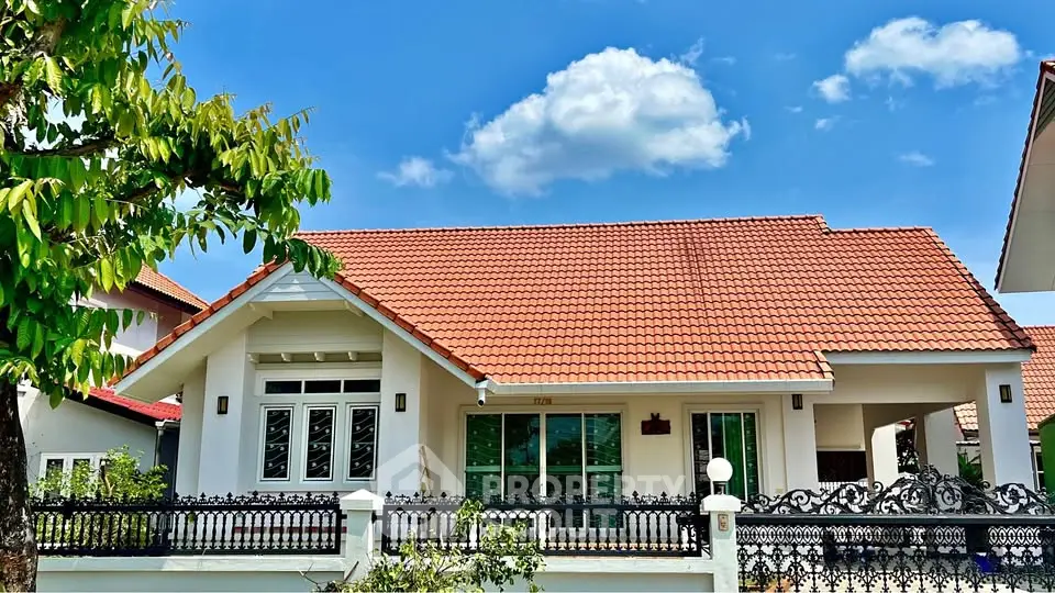 Charming single-story house with red-tiled roof and lush garden under a clear blue sky.