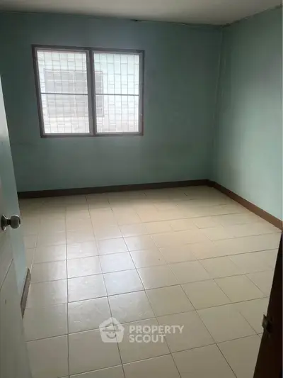 Spacious empty room with tiled flooring and large window, ideal for customization.