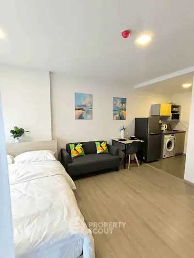 Modern studio apartment with cozy living area and compact kitchen featuring washing machine and fridge.