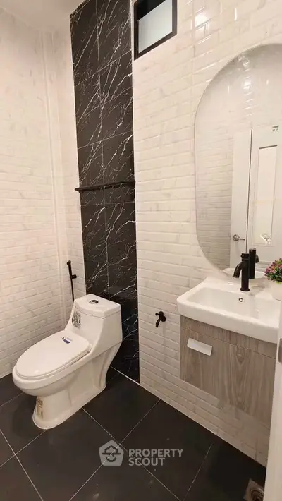 Modern bathroom with sleek black and white tiles, featuring a stylish oval mirror and contemporary fixtures.