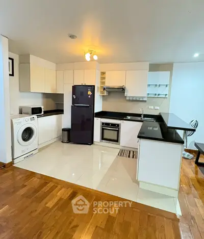 Modern kitchen with sleek black countertops, built-in oven, and washing machine in open layout.
