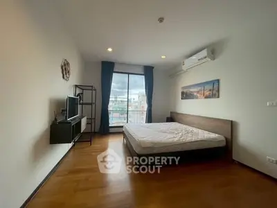 Spacious bedroom with large window and city view, featuring modern furnishings and wooden flooring.