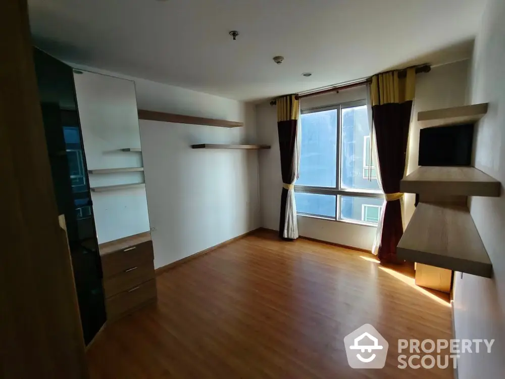 Spacious empty room with wooden flooring and large window, ideal for customization.