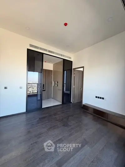 Spacious modern room with dark wood flooring and large windows offering city views.