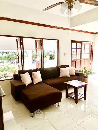 Spacious living room with modern brown sofa and natural light from large windows.