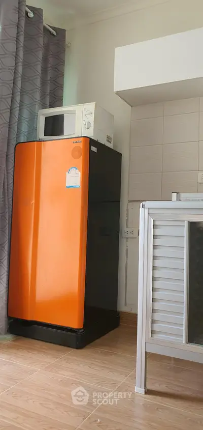 Compact kitchen corner with orange fridge and microwave, ideal for modern apartments.