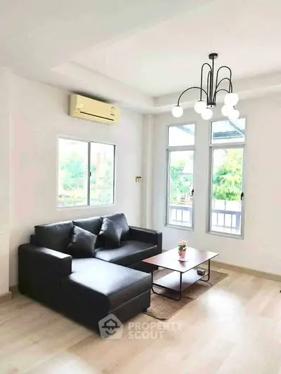 Modern living room with sleek black sofa, stylish lighting, and large windows offering natural light.