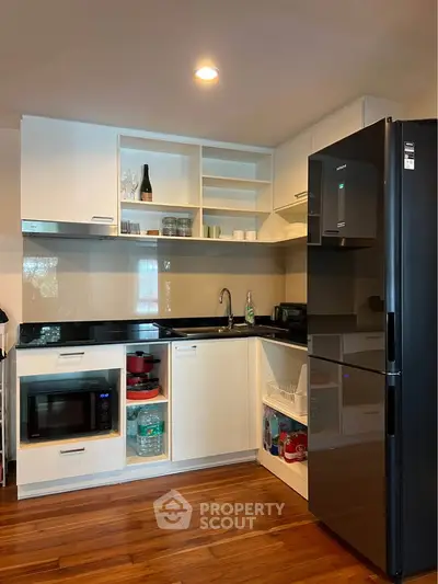 Modern kitchen with sleek black fridge, microwave, and ample storage in a stylish apartment.