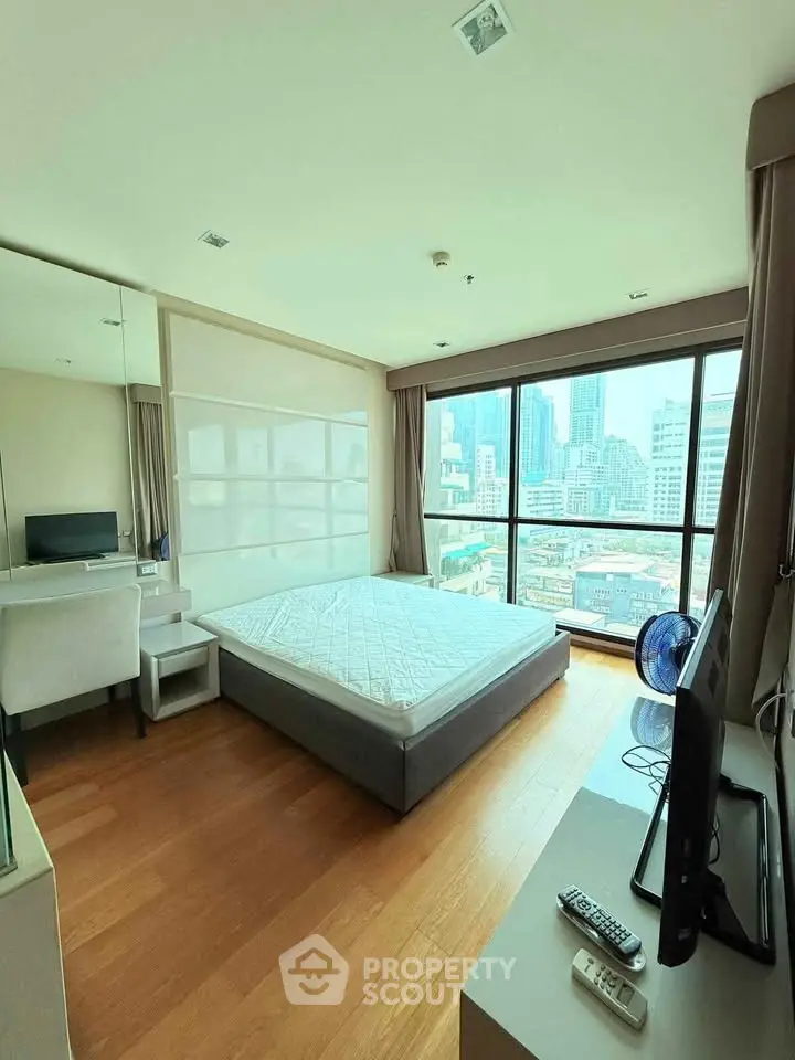Modern bedroom with city view, featuring a large window and sleek furnishings.