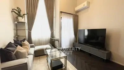 Modern living room with sleek furniture and large TV, featuring elegant curtains and air conditioning.