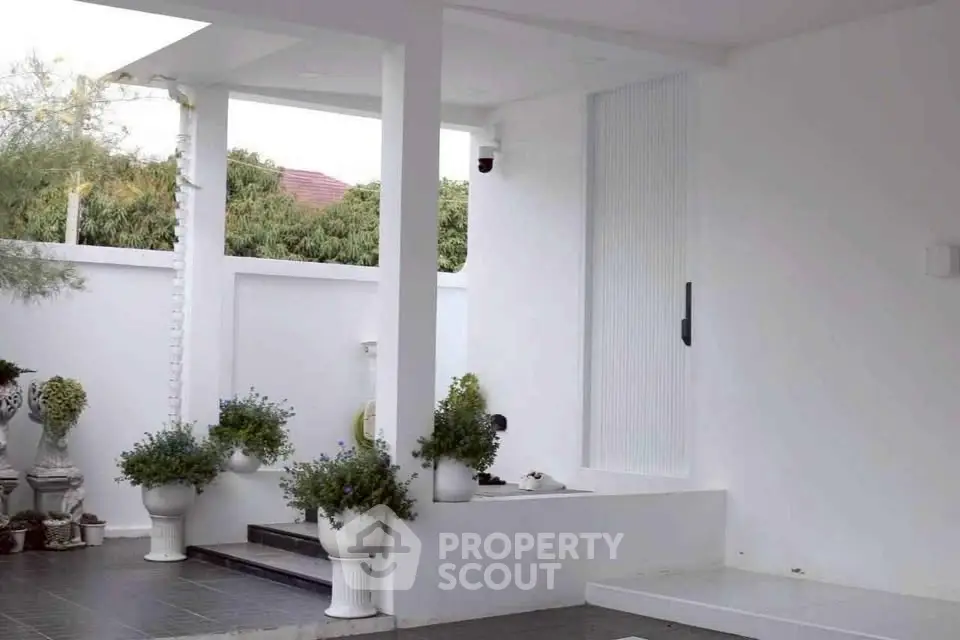 Elegant modern exterior with white walls and lush greenery, perfect for serene outdoor living.