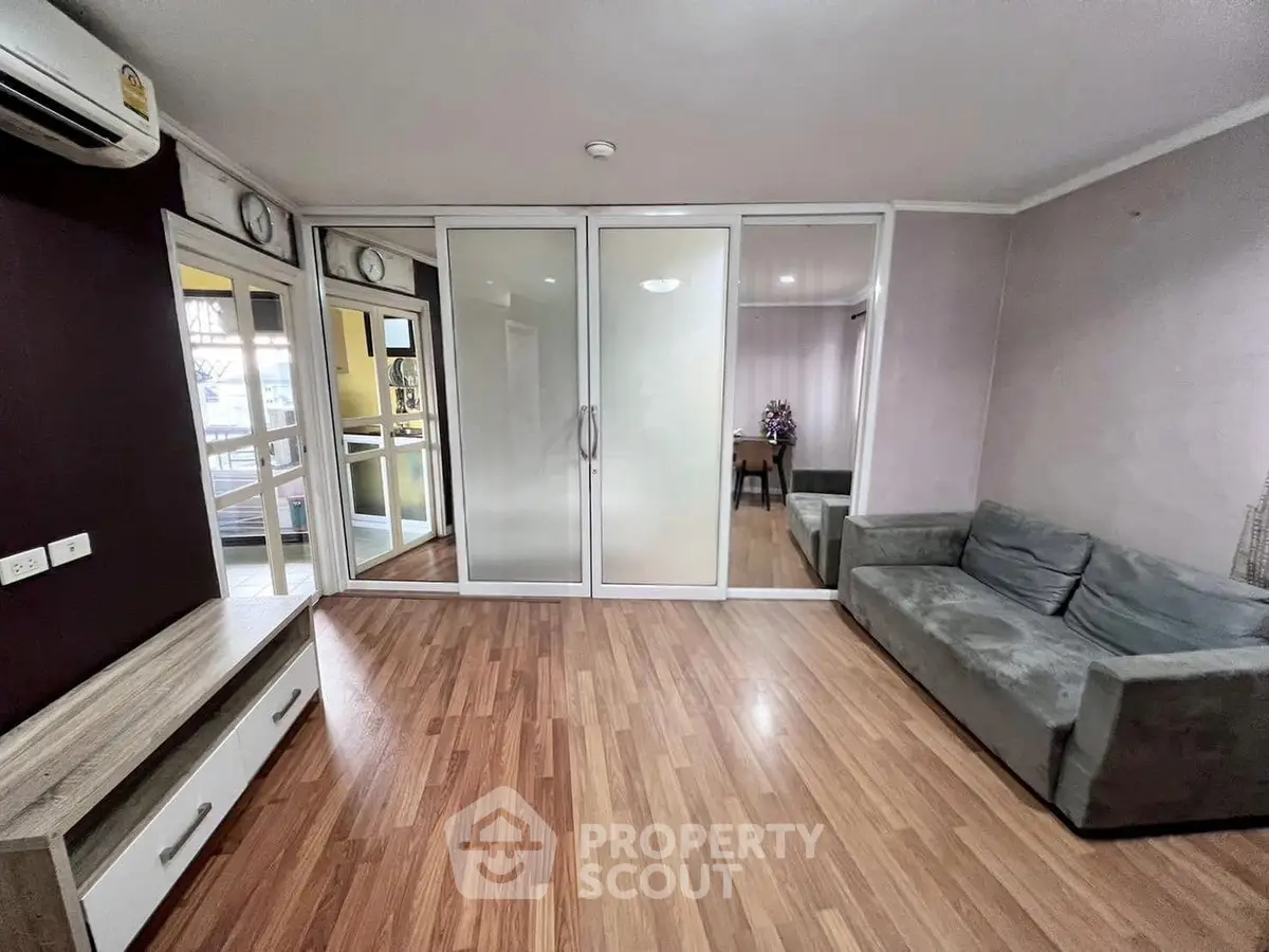 Spacious living room with wooden flooring and modern glass partitions in a stylish apartment.
