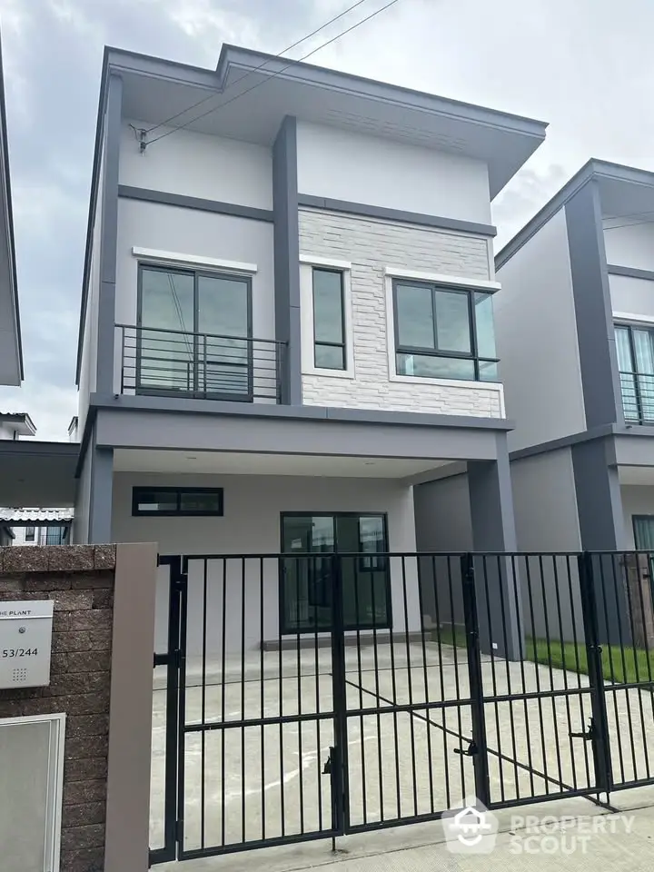 Modern two-story house with sleek design and gated driveway in suburban neighborhood.