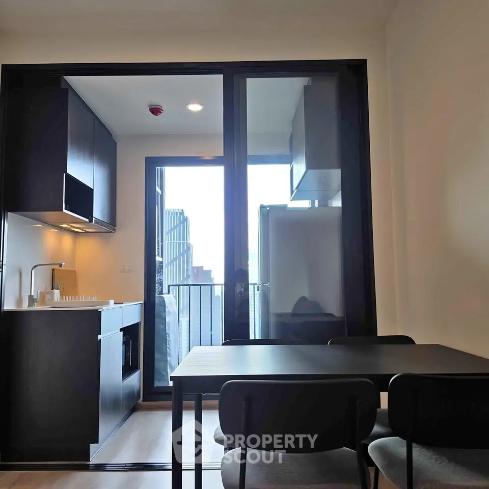 Modern kitchen with sleek black cabinetry and dining area, featuring a balcony view in a contemporary apartment.